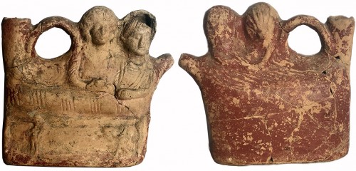 Argilla terra di Siena depuratissima; decorazione a vernice rossa stesa su tutta la superficie dell’askòs, ad eccezione delle vesti in cui risalta un colore rosato, mentre non è conservata, neppure in tracce, la cromia sui volti e la capigliatura dei personaggi.
Tecnica a matrice duplice.
Dimensioni: lungh, cm 19,3; alt. cm 17, 7; largh. cm 6, 7.